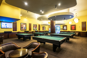 Pool tables in a room with football t-shirts in frames and a TV showing a football game